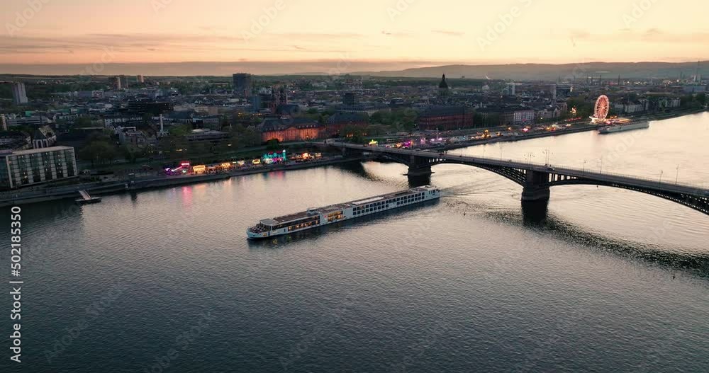 Sunset drone flight over Mainz at the Rhine river with a boat and the main city bridge in front of orange sky with a summer wine festival in the back Sunset drone flight over Mainz at the Rhine river with a boat and the main city bridge in front of orange sky with a summer wine festival in the back