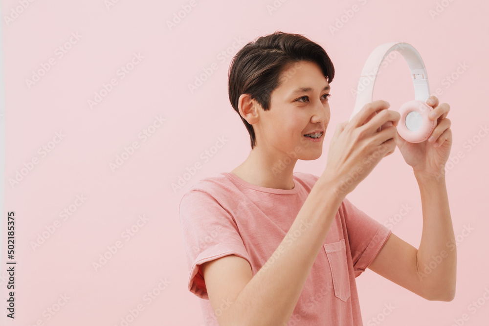 Asian boy wearing t-shirt smiling while posing with headphones Asian boy wearing t-shirt smiling while posing with headphones