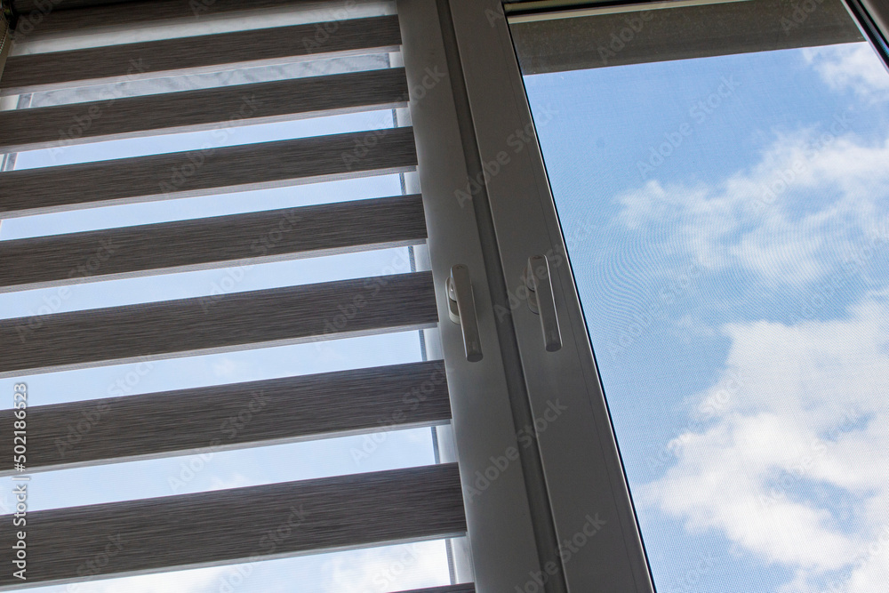 a plastic window with a roller blind and a mosquito net against a blue sky a plastic window with a roller blind and a mosquito net against a blue sky