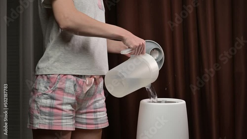 A young woman pours water into an air humidifier and steam starts coming out of the nozzle
