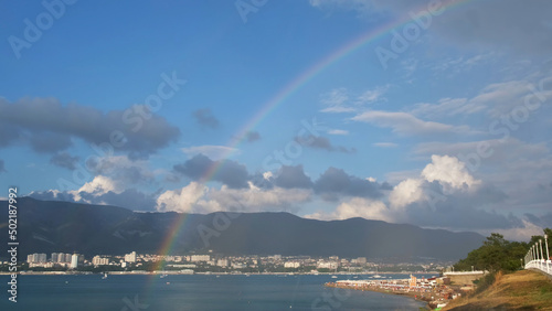 Breathtaking view of rainbow touches the sea during the rain in a small town at the Black sea. Concept. Summer marine landscape on blue cloudy sky background.