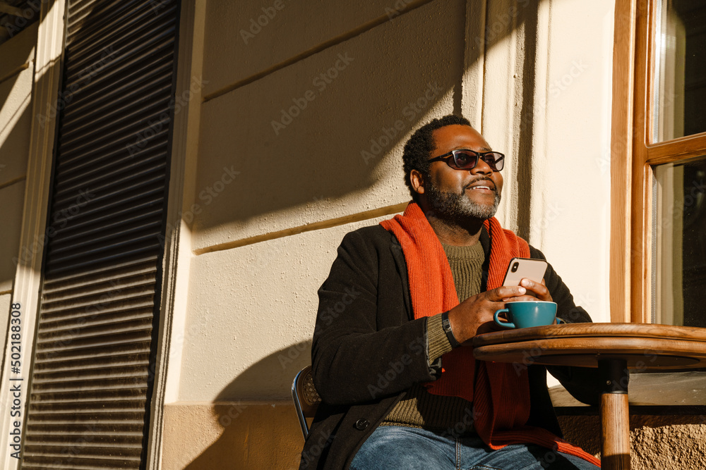 Black man using cellphone and drinking coffee while sitting in cafe Black man using cellphone and drinking coffee while sitting in cafe