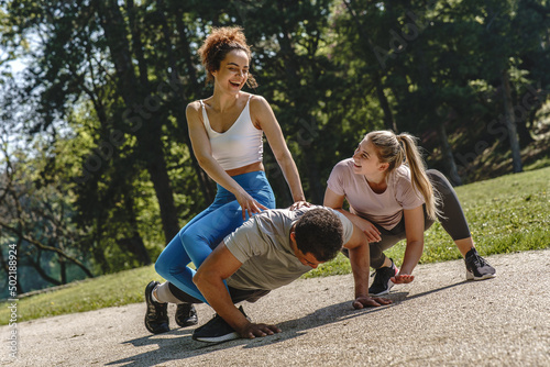 Young people workout at the park. Man doing push ups and his female friends cheering him up. © BalanceFormCreative
