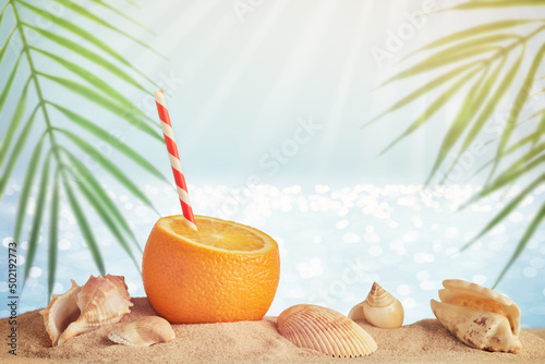 Fototapeta Naklejka Na Ścianę i Meble -  Summer travel concept with creative orange cocktail and beach. Blurred sea background with palm leaves, sand and seashells
