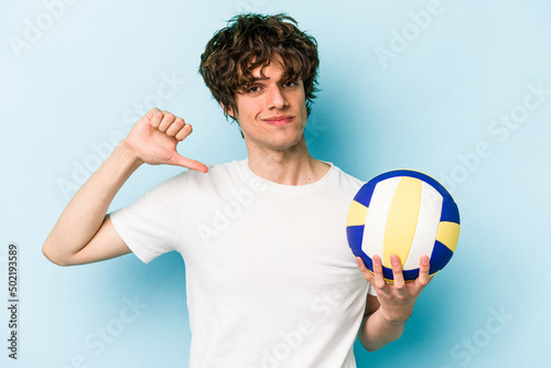 Young caucasian man playing volleyball isolated on blue background feels proud and self confident, example to follow.