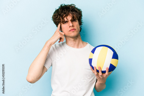 Young caucasian man playing volleyball isolated on blue background pointing temple with finger, thinking, focused on a task.