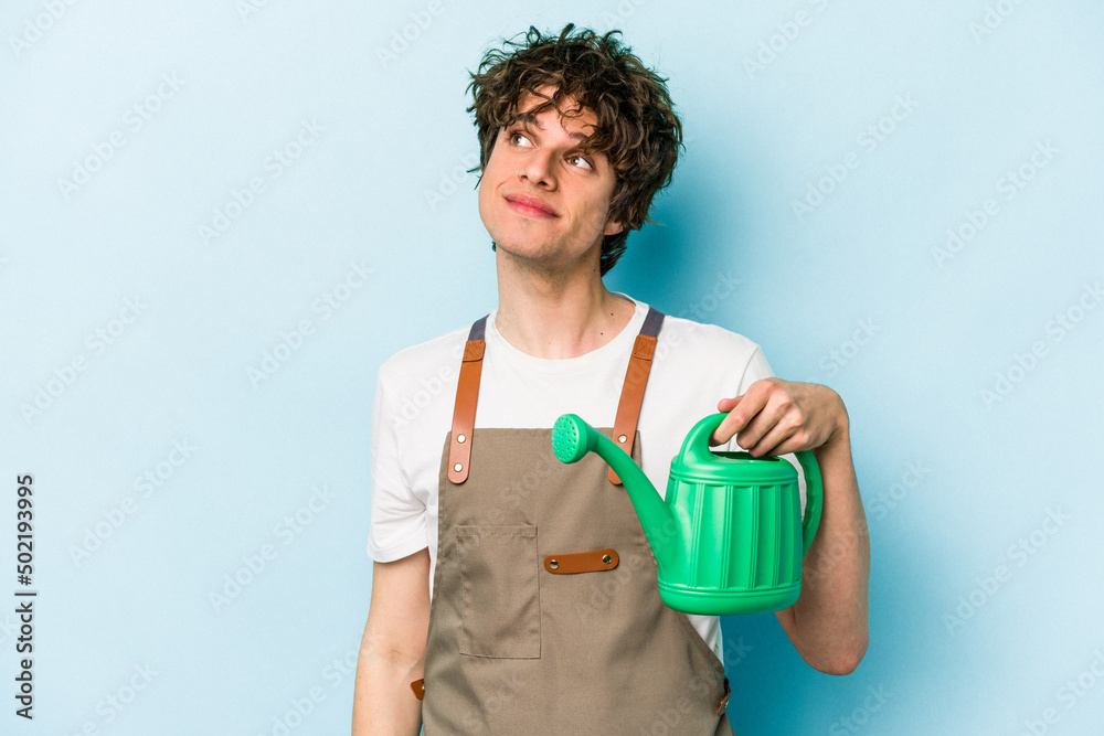 Young gardener caucasian man holding watering can isolated on blue background dreaming of achieving goals and purposes