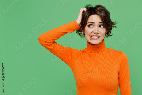 Young puzzled mistaken pensive sad woman 20s wear casual orange turtleneck look aside scratch hold head isolated on plain pastel light green color background studio portrait. People lifestyle concept. photo