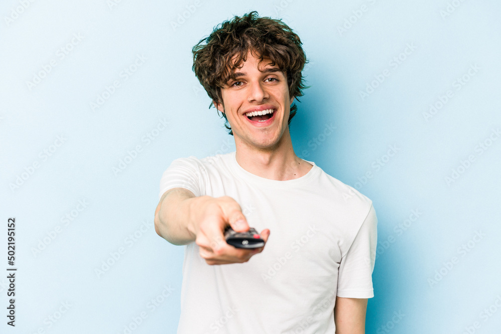 Young caucasian man holding tv controller isolated on blue background Young caucasian man holding tv controller isolated on blue background