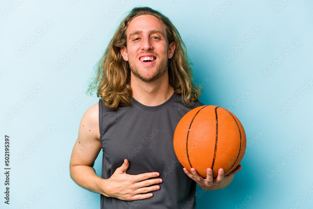 Young caucasian man playing basketball isolated on blue background laughing and having fun.
