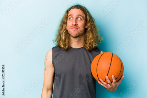 Young caucasian man playing basketball isolated on blue background dreaming of achieving goals and purposes