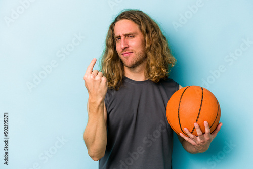 Young caucasian man playing basketball isolated on blue background pointing with finger at you as if inviting come closer.