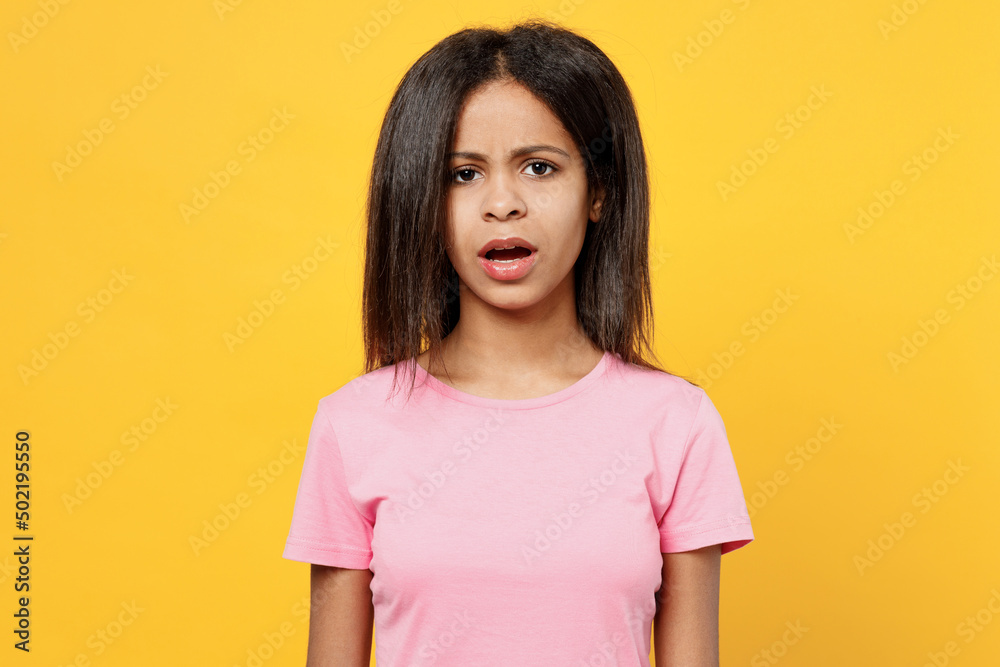 Fototapeta premium Little disappointed sad worried kid girl of African American ethnicity 12-13 years old wear pink t-shirt look camera isolated on plain yellow background studio portrait. Childhood lifestyle concept.