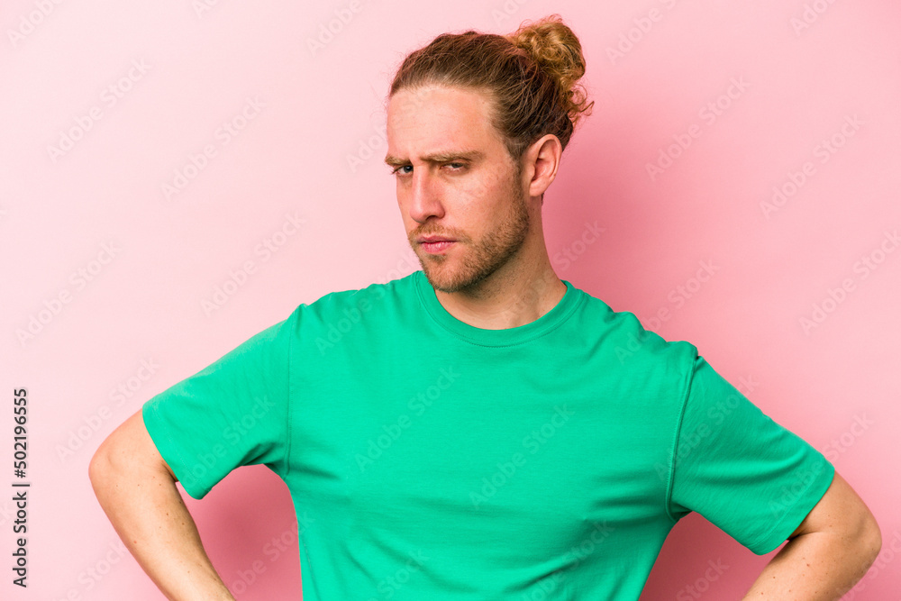 Young caucasian man isolated on pink background frowning face in displeasure, keeps arms folded.