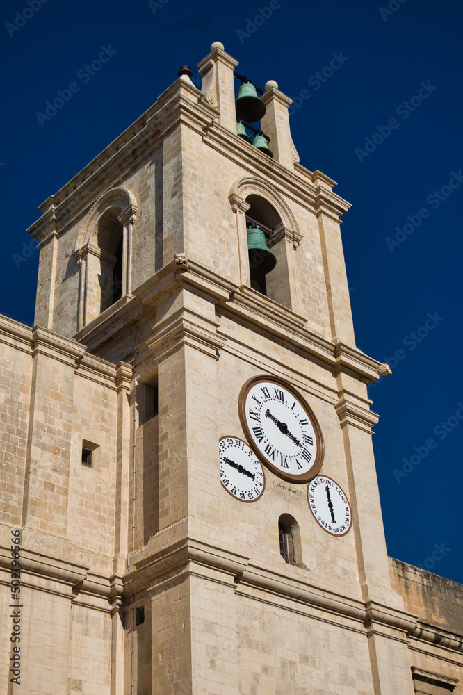 Church tower in Malta with multiple clocks on it in front of a clear dark blue sky on a sunny day. Vacation feeling. 