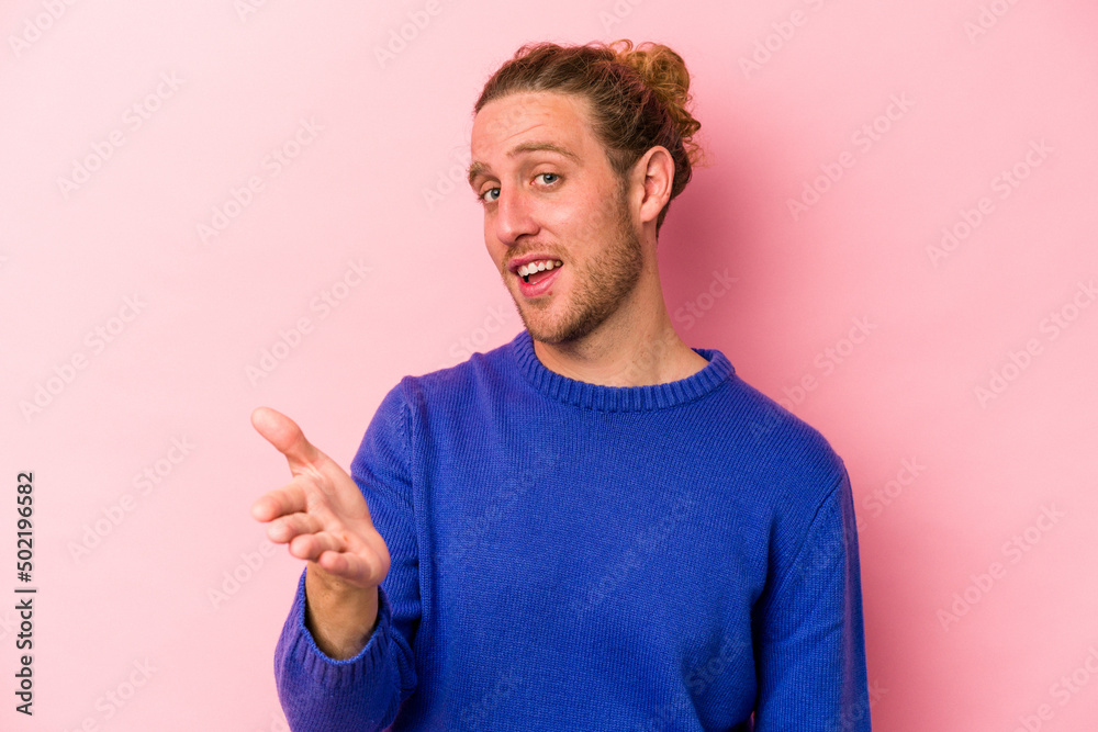 Young caucasian man isolated on pink background stretching hand at camera in greeting gesture. Young caucasian man isolated on pink background stretching hand at camera in greeting gesture.