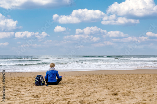 Fototapeta Naklejka Na Ścianę i Meble -  Meditation by the sea. Woman sitting on the beach practicing meditation observing the horizon of the sea. Concept of spirituality, meditation and inner growth.