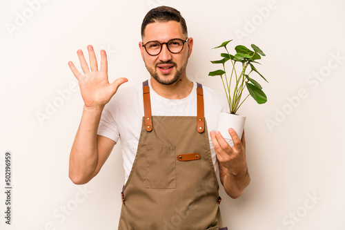Hispanic gardener man holding a plant isolated on white background smiling cheerful showing number five with fingers.