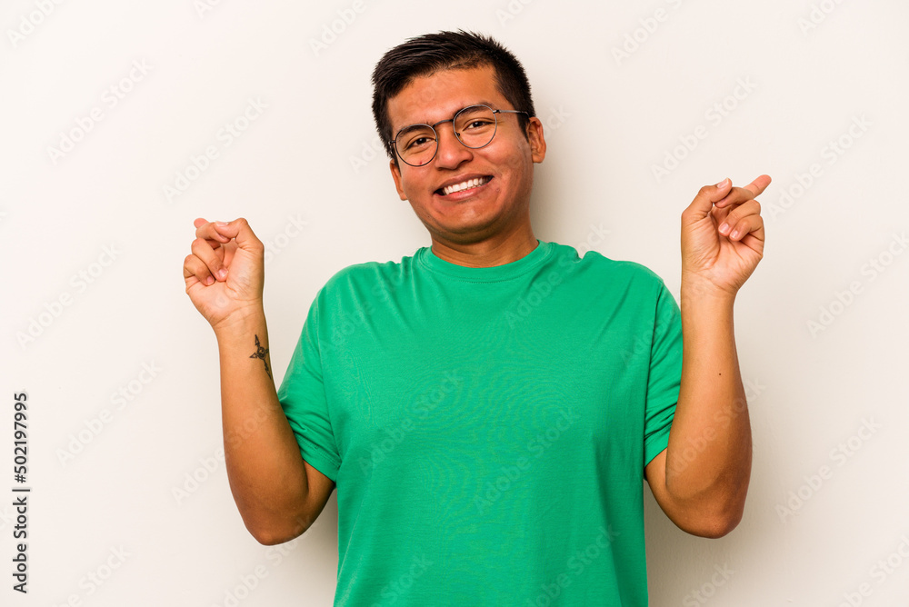 Fototapeta premium Young hispanic man isolated on white background pointing to different copy spaces, choosing one of them, showing with finger.
