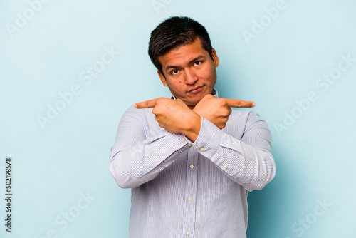 Young hispanic man isolated on blue background points sideways, is trying to choose between two options.