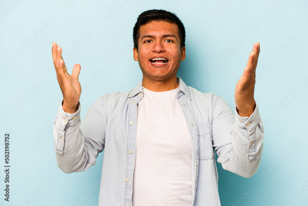Young hispanic man isolated on blue background celebrating a victory or success, he is surprised and shocked.