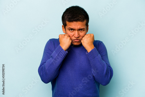 Young hispanic man isolated on blue background showing fist to camera, aggressive facial expression.