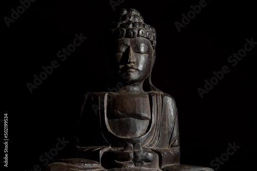 Sitting buddha statue in lotus position. It is made of palm wood. Dark Image, Copy Space.