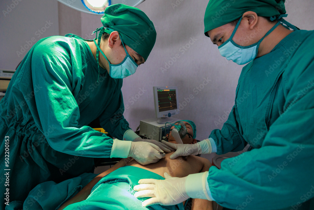 Two Asian surgeons doctor working together on a surgery with male patient  in operation room.