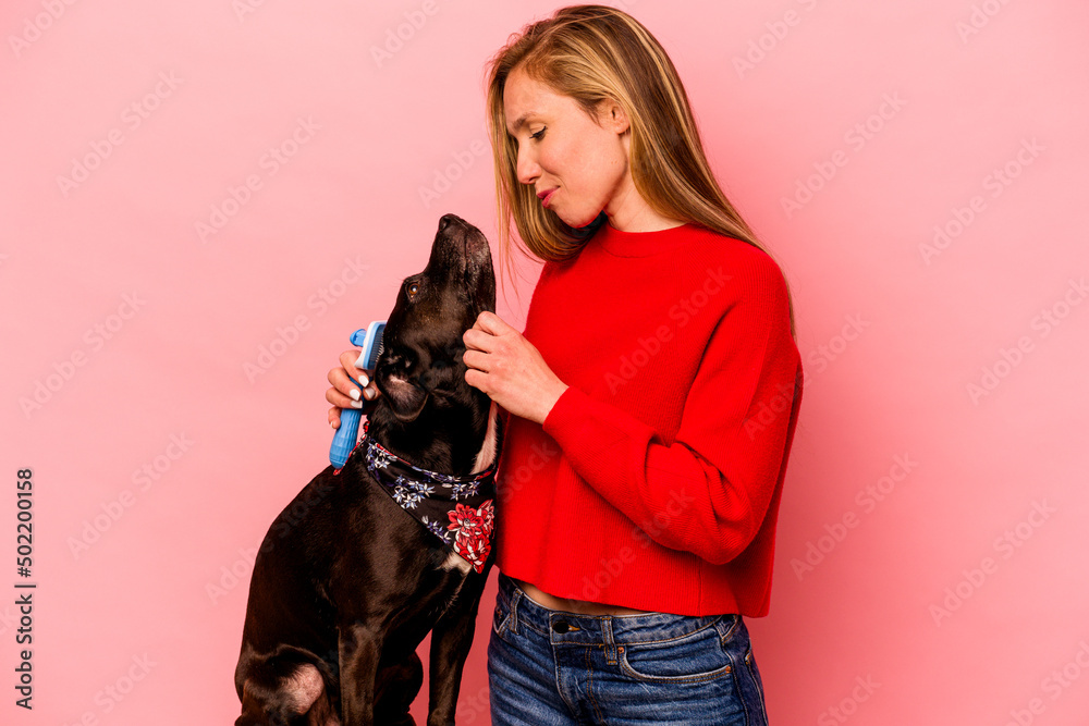 Young caucasian woman combing the dog isolated on pink background Young caucasian woman combing the dog isolated on pink background