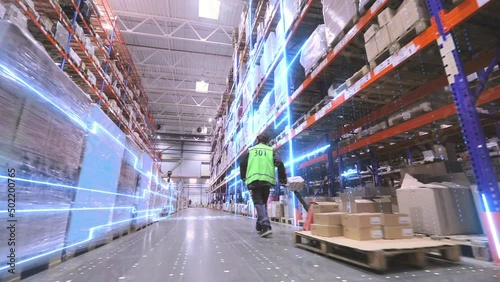A worker is carrying a rokla through a large warehouse. The worker walks through the warehouse. Digitalization of production. Futuristic production concept.