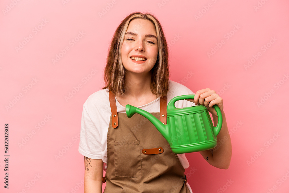 Young gardener woman holding watering can isolated on pink background laughing and having fun. Young gardener woman holding watering can isolated on pink background laughing and having fun.