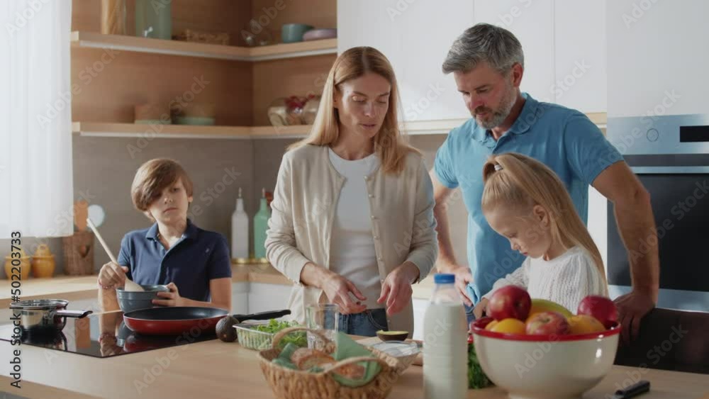 Caucasian family with little kids prepare together healthy vegetable salad in the kitchen at home. Parents teach little daughter healthy habits and how to cut avocado. Caucasian family with little kids prepare together healthy vegetable salad in the kitchen at home. Parents teach little daughter healthy habits and how to cut avocado.