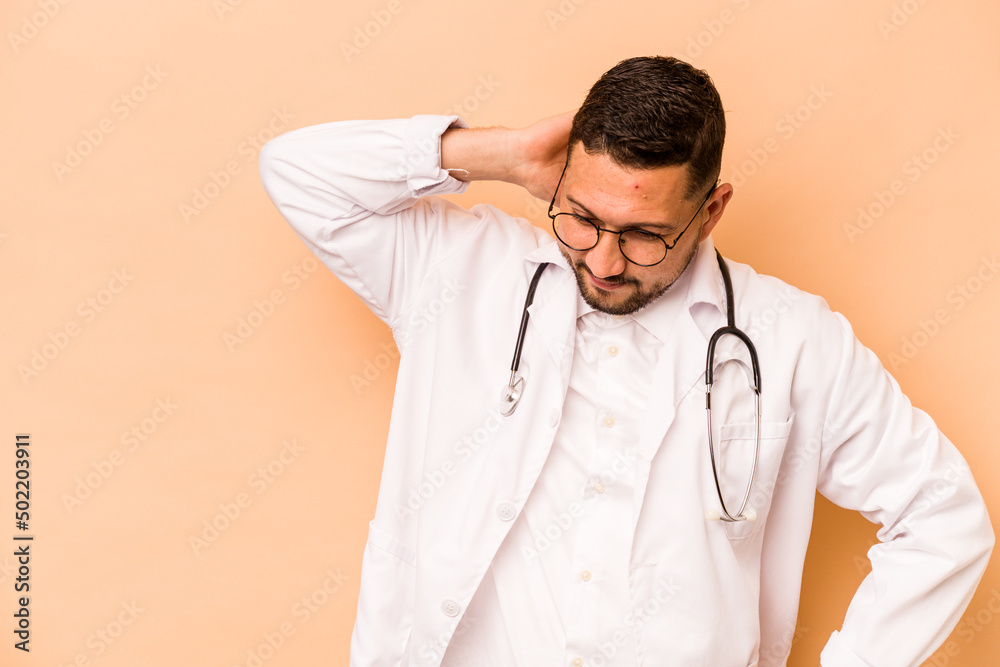 Hispanic doctor man isolated on beige background touching back of head, thinking and making a choice.