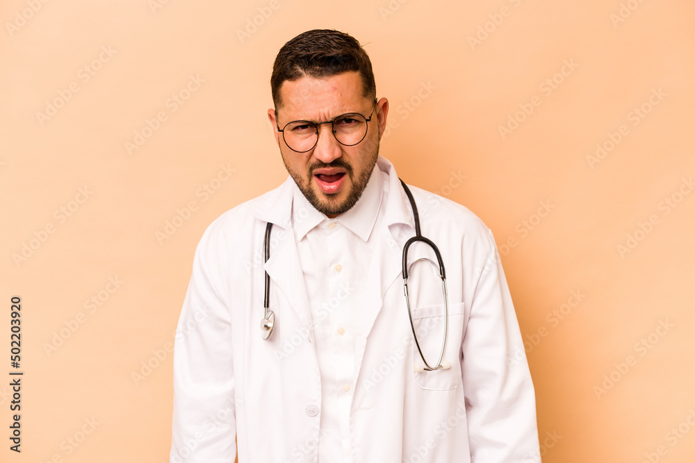 Hispanic doctor man isolated on beige background screaming very angry and aggressive. Hispanic doctor man isolated on beige background screaming very angry and aggressive.