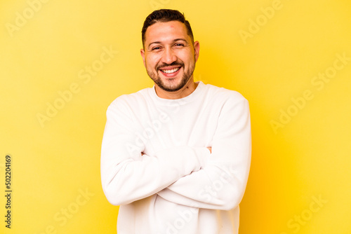 Young hispanic man isolated on yellow background who feels confident, crossing arms with determination.