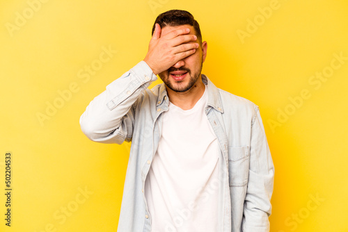 Young hispanic man isolated on yellow background covers eyes with hands, smiles broadly waiting for a surprise. © Asier