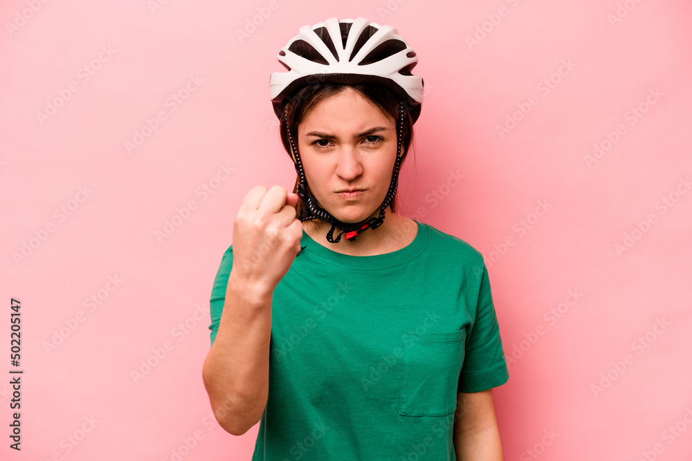 Young caucasian woman wearing helmet isolated on pink background showing fist to camera, aggressive facial expression. Young caucasian woman wearing helmet isolated on pink background showing fist to camera, aggressive facial expression.