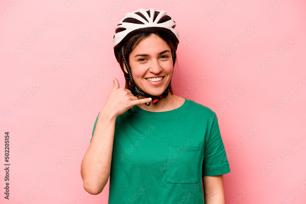 Young caucasian woman wearing helmet isolated on pink background showing a mobile phone call gesture with fingers. Young caucasian woman wearing helmet isolated on pink background showing a mobile phone call gesture with fingers.