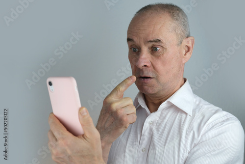 close-up of mature charismatic man looks at screen of phone in pink cover, senior 60 years surprised, shocked by news, event, bright facial expressions, overhang, concept human stress resistance photo