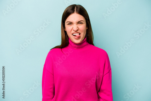 Young caucasian woman isolated on blue background funny and friendly sticking out tongue. © Asier