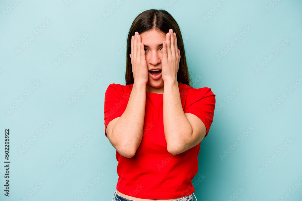 Young caucasian woman isolated on blue background having fun covering half of face with palm. Young caucasian woman isolated on blue background having fun covering half of face with palm.