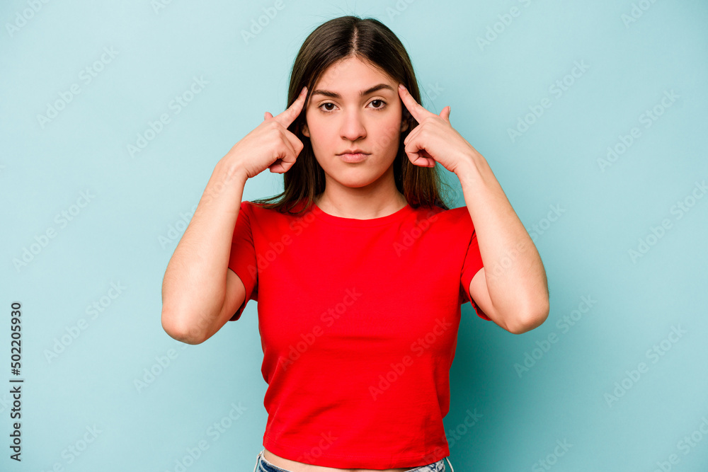 Young caucasian woman isolated on blue background focused on a task, keeping forefingers pointing head.