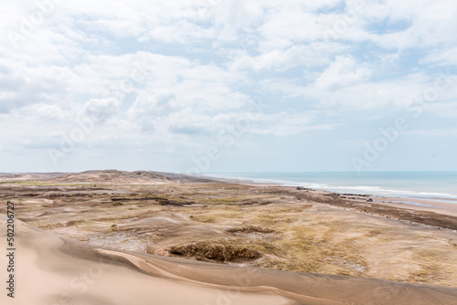 View of the sand and dunes in front of the sea with some clouds in the sky. 