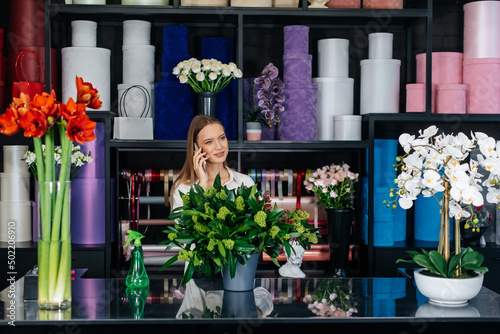 A young woman florist accepts an order by phone for the production of a beautiful festive bouquet. Floristry and making of bukets in a flower shop. Small business.