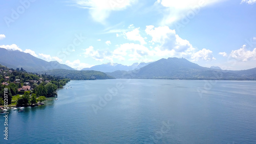 Panorama of lake, mountains and cottages near shore. Action. Top view of picturesque blue lake, shore with cottages for country holiday in summer and mountains on horizon