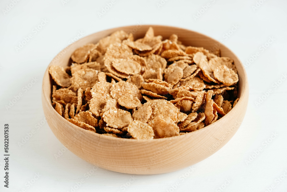 Crispy healthy dry cereal flakes in a wooden bowl on white background Crispy healthy dry cereal flakes in a wooden bowl on white background