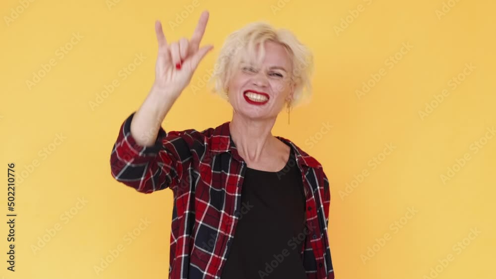 Horn gesture. Rocker woman. Exciting joy. Funny middle-aged lady enjoying punk music showing hands sign dancing isolated yellow. Horn gesture. Rocker woman. Exciting joy. Funny middle-aged lady enjoying punk music showing hands sign dancing isolated yellow.
