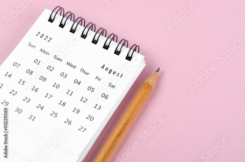 August 2022 desk calendar with wooden pencil on pink background.