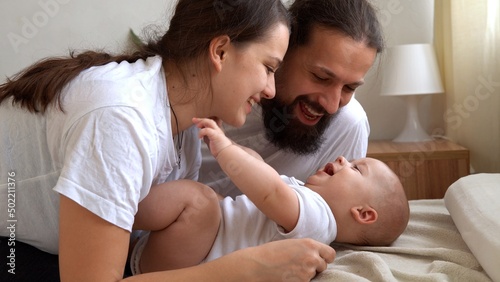 Woman And Man Holding Newborn. Mom, Dad And Baby On Bed. Close-up. Portrait of Young Smiling Family With Newborn On Hands. Happy Marriage Couple On Background. Childhood, Parenthood, Infants Concept