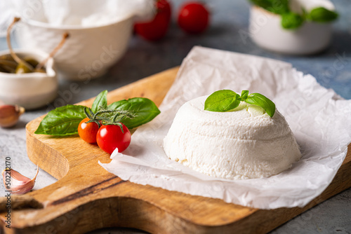 Homemade Italian ricotta cheese or cottage cheese with basil ready to eat. Vegetarian healthy, nutritious diet food on wooden background photo